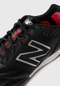 Μαύρο ποδοσφαιρικό παπούτσι με συνθετικό επάνω μέ�ρος, ασημί λεπτομέρειες, κόκκινες διακοσμήσεις, υφή επιφάνειας και μαύρα κορδόνια. Ο αριθμός μοντέλου 442 είναι ορατός στο πλάι.