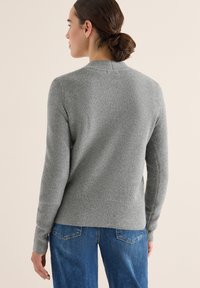 Grauer, gerippter Pullover mit langen Ärmeln, Rundhalsausschnitt und strukturiertem Stoff. Getragen mit blauen Jeans, die von hinten eine figurbetonte Passform zeigen.