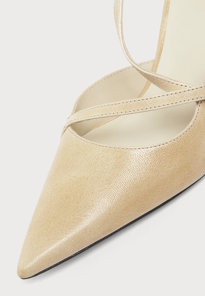 Chaussure en cuir beige à bout pointu avec fines lanières croisées et une semelle intérieure lisse sur fond blanc.