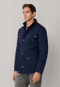 Marinebl�å quiltet jakke med stand-up krave, sølvfarvede trykknapper og to forlommer. Har et struktureret stof og en afslappet pasform.