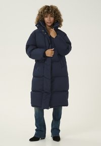 Abrigo acolchado de la marina con cuello alto, cierres a presión y diseño acolchado. Combina con jeans acampanados y botines negros.