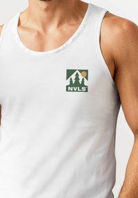 Weiße Tanktop mit einem rechteckigen Logo, das grüne Bäume, Berge und eine Sonne zeigt. Der Stoff wirkt glatt und enganliegend.