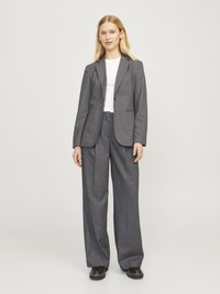 Blazer gris a medida combinado con pantalones anchos grises. El material parece tejido; textura suave con un brillo sutil. Camiseta blanca casual por debajo.