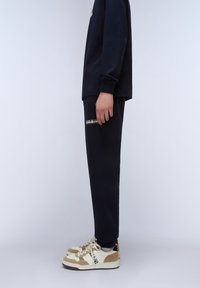 Marineblaues Langarmshirt, passende Hose und beigefarbene Sneakers mit braunen Akzenten. Die Hose verfügt über ein Logodetail am Saum. Glatte Stoffoberfläche.