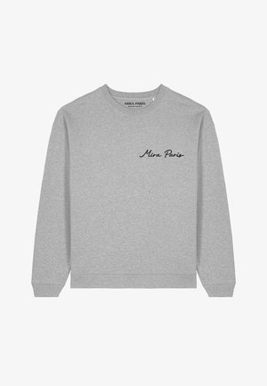 Jeune homme portant un sweat-shirt gris clair à col rond avec "Mira Paris" brodé sur la poitrine, face à droite sur un fond uni.