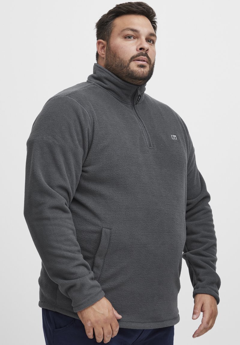 Grau Fleece-Pullover mit hohem Kragen, halber Reißverschluss und Seitentaschen. Weiche Textur und lockere Passform, mit kleinem Logo auf der Brust.