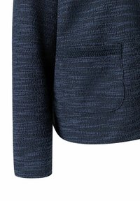 Marineblauwe blazer van textuur met een geweven stof. Voorzien van een enkele pocket en een iets taps toelopende mouw, die eindigt bij de pols.