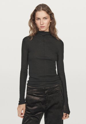 Haut noir à manches longues avec col roulé en tissu doux et fin, au design ajusté et aux détails de couture, associé à un pantalon en velours côtelé foncé.