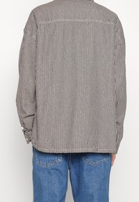 Camicia a maniche lunghe a righe in tessuto di cotone marrone e bianco, con vestibilità morbida, polsini con bottoni e un dettaglio a yoke sul retro.