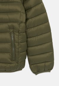 Olivovo zelená puffa bunda s rukávom s prešívanou textúrou. Obsahuje zipsovú kapsu a elastické manžety. Materiál vyzerá hladko a ľahko.