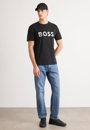Schwarzes Baumwoll-T-Shirt mit dem Wort "BOSS" in einem Rastermuster, kombiniert mit blauen geraden Jeans und schwarzen Sneakern.