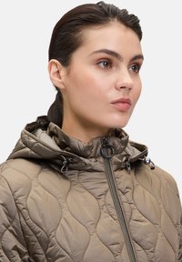 Veste matelassée olive avec un col haut, fermeture éclair sur le devant et capuche ajustable. Présente une texture lisse et brillante ainsi que des coutures décoratives.