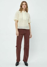 Krämfärgad stickad blus med zigzag-mönster, korta puffärmar och knapprad. Matchad med bruna rakbenade byxor och svarta stövlar.