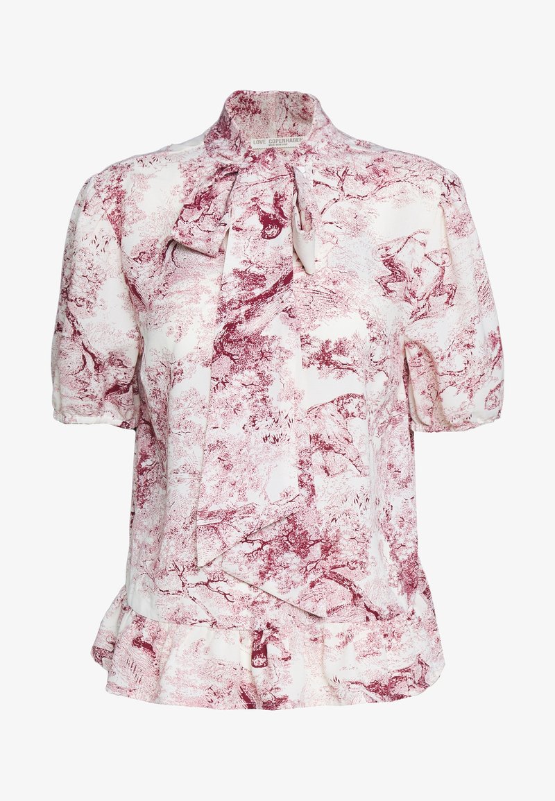 Blouse blanche avec imprimé abstrait nature rouge, manches courtes bouffantes, ourlet à volants et grand nœud papillon au col montant.