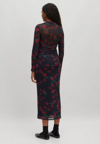 Langärmliges, figurbetontes Kleid aus transparenter navyblauer Stoff mit rotem Rosenmuster. Raffung im Rücken, midi-lange, kombiniert mit schwarzen Ballerinas.