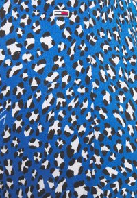 Luipaardprint stof in blauw, zwart en wit, met een gestructureerd oppervlak met kleine vlekken en een subtiele merklogo in rood en wit.