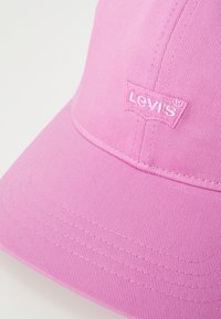 Rózsaszín sapka texturált anyagból, ívelt napernyővel. Kontrasztos színű hímzett "Levi's" logóval a fronton.