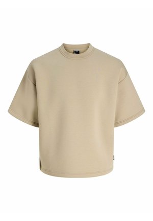T-shirt beige oversize à manches courtes avec col rond, épaules tombantes et petite étiquette noire sur la couture latérale.