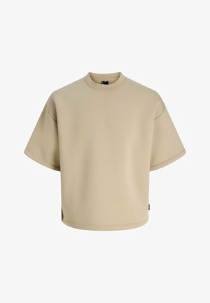 T-shirt beige oversize à manches courtes avec col rond, épaules tombantes et petite étiquette noire sur la couture latérale.