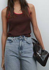 Bruine geribbelde tanktop met rode accenten, gecombineerd met hooggeknipte lichtblauwe denim jeans. Een donkere leren tas steunt tegen de taille.