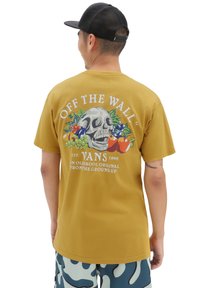 Camiseta de algodón amarilla con un diseño de calavera y acentos florales en la parte posterior, y el texto "OFF THE WALL" en blanco encima.