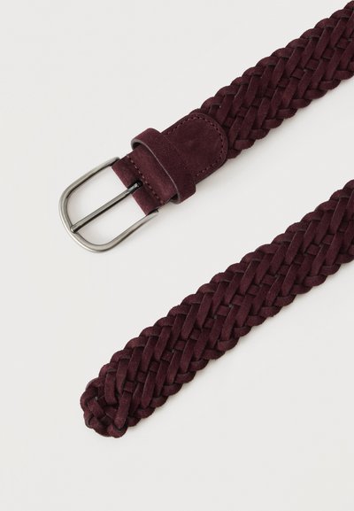 Ceinture en daim tressé bordeaux foncé avec boucle et passant en métal argenté sur un fond uni clair.