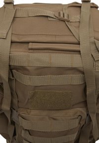 Sac à dos tactique beige avec plusieurs sangles, boucles et un patch Velcro à l'avant, conçu pour un port et une fixation sécurisés.