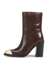 Botas de tornozelo em pele castanha com um salto robusto, apresentando uma ponta em aço texturizada dourada e um acabamento suave. Costura lateral com um pequeno detalhe de metal.