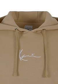 Beige mikina s kapucí a šňůrkou, s bílým vyšívaným textem; měkká textura, volný střih a minimalistický design.