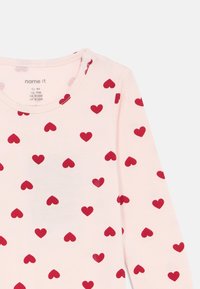Lichtroze peuter T-shirt met lange mouwen en een patroon van rode harten, ronde halslijn en maatlabel dat EU 80, US 12M, CA 9-12M, UK 9-12M aangeeft.