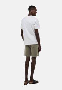 T-shirt en coton blanc, à manches courtes, associé à un short vert olive, avec une poche arrière. Des sandales noires à enfiler complètent l'ensemble.