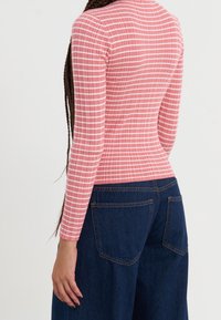 Dlouhý rukáv, přiléhavý top v růžové barvě s bílými horizontálními pruhy, zkombinovaný s vysokým pasem a širokými tmavě modrými džínami, které mají dvě zadní kapsy.