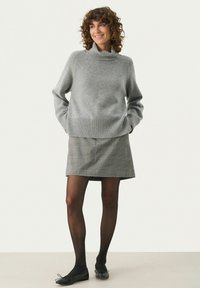 Grå strikket sweater med høj krave, parret med en ternet mini nederdel. Modellen har sorte strømpebukser og balletflader på.
