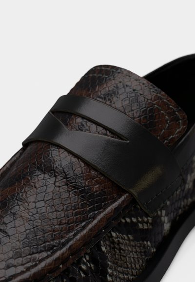 Κοντινό πλάνο μοκασίνου με υφή φολίδων φιδ ιού σε σκουρό καφέ και μαύρο χρώμα, με λεία μαύρη δερμάτινη λωρίδα στο πάνω μέρος.