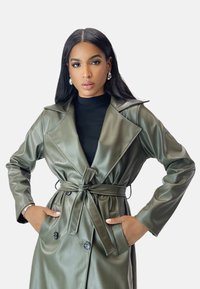 Olivenfarbener Kunstleder-Trenchcoat mit großen Revers, tailliertem Gürtel und Knopf-Details, langen Ärmeln und Seitentaschen.