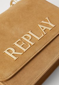 Borsa in suede beige con un grande logo dorato "REPLAY". Texture liscia con cuciture pulite e un design piatto. Accenti in metallo.