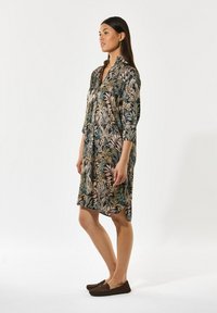 Blumendruckkleid mit Kragen, Dreiviertelärmeln und asymmetrischem Saum. Hergestellt aus leichtem Stoff in dunklen Tönen.