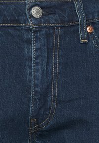 Tmavě modré džíny z denimu s pozlaceným švem, stříbrným zapínáním na knoflík a klasickým designem s předními kapsami.