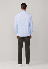 Camicia a righe blu chiaro in tessuto, con colletto button-down e maniche lunghe. Abbinata a pantaloni verde oliva e sneakers bianche.