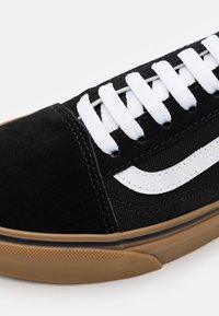 Sneaker nera con tomaia in suede e tela, lacci bianchi e logo laterale bianco. Include una suola in gomma marrone con un motivo testurizzato.