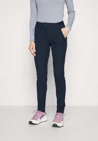 Pantaloni stretch blu navy con una vestibilità slim, dotati di tasca frontale, chiusura a bottone metallico e texture morbida. Abbinati a scarpe da ginnastica rosa chiaro.