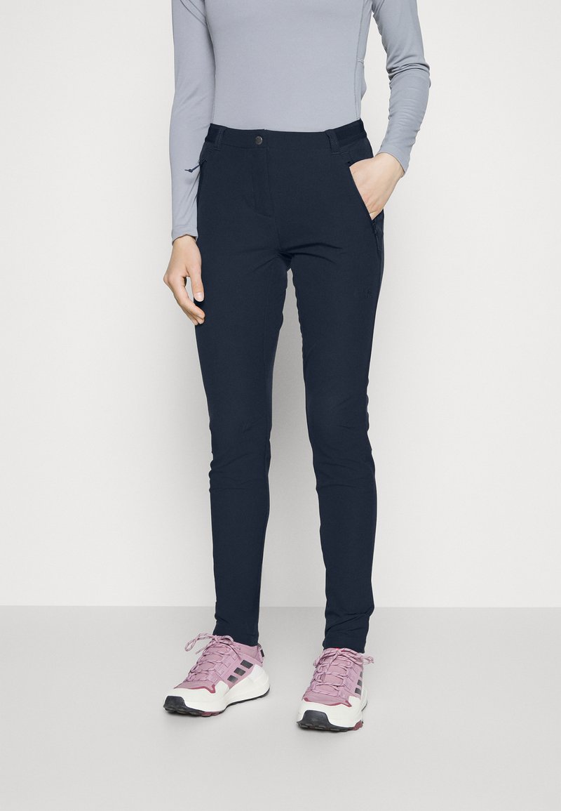 Pantaloni stretch blu navy con una vestibilità slim, dotati di tasca frontale, chiusura a bottone metallico e texture morbida. Abbinati a scarpe da ginnastica rosa chiaro.