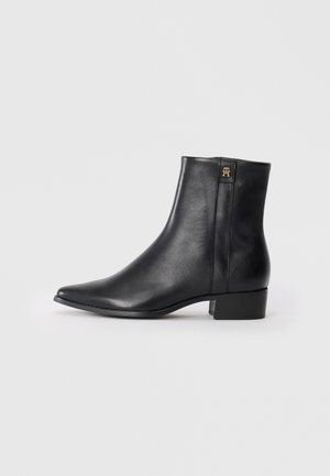 Bottines en cuir noir avec un bout pointu, texture lisse, petit talon carré et un logo doré sur le côté.