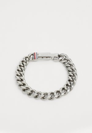 Sølvmetallkjedearmbånd med store sammenkoblede lenker. Har en lås med et lite rødt, hvitt og blått accent. Polert overflate.