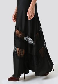 Zwarte jurk met gelaagd ontwerp en doorschijnende kantinzetten. Soepele stof, asymmetrische zoom, gecombineerd met bordeauxrode stiletto-hakken.
