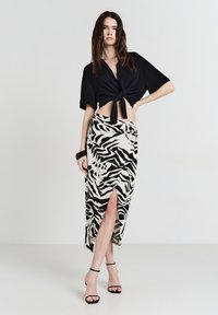 Camicetta nera a maniche corte con bottoni annodata in vita, abbinata a una gonna zebrate beige e nera con spacco anteriore e tessuto testurizzato.