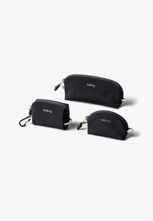 Trois pochettes zippées noires Bellroy de différentes tailles, dont une avec un clip, disposées sur un fond blanc.