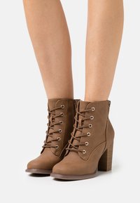 Brązowe ankle boots z imitacji skóry z sznurówką z przodu, metalowymi oczkami i teksturowanym obcasem, z bocznym zamkiem błyskawicznym dla łatwego zakupu.