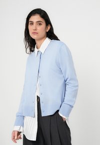 Γαλάζια ζακέτα με στρογγυλή λαιμόκοψη, μακριά μανίκια και κούμπωμα με κουμπιά. Φτιαγμένη από μαλακό υλικό, με ριμπ μανσέτες και κάτω μέρος.