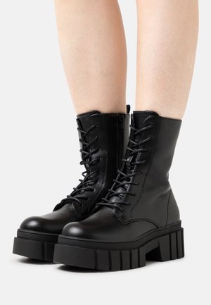 Black leather combat boots with thick, ridged black sole, lace-up front and zipper detail on the side, featuring a rounded toe and sturdy design.